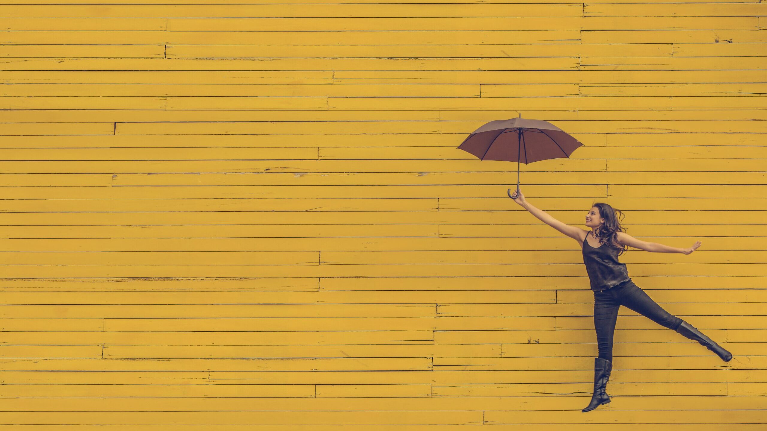 黄色い壁をバックに女性が傘をさして空を飛んでいる写真
